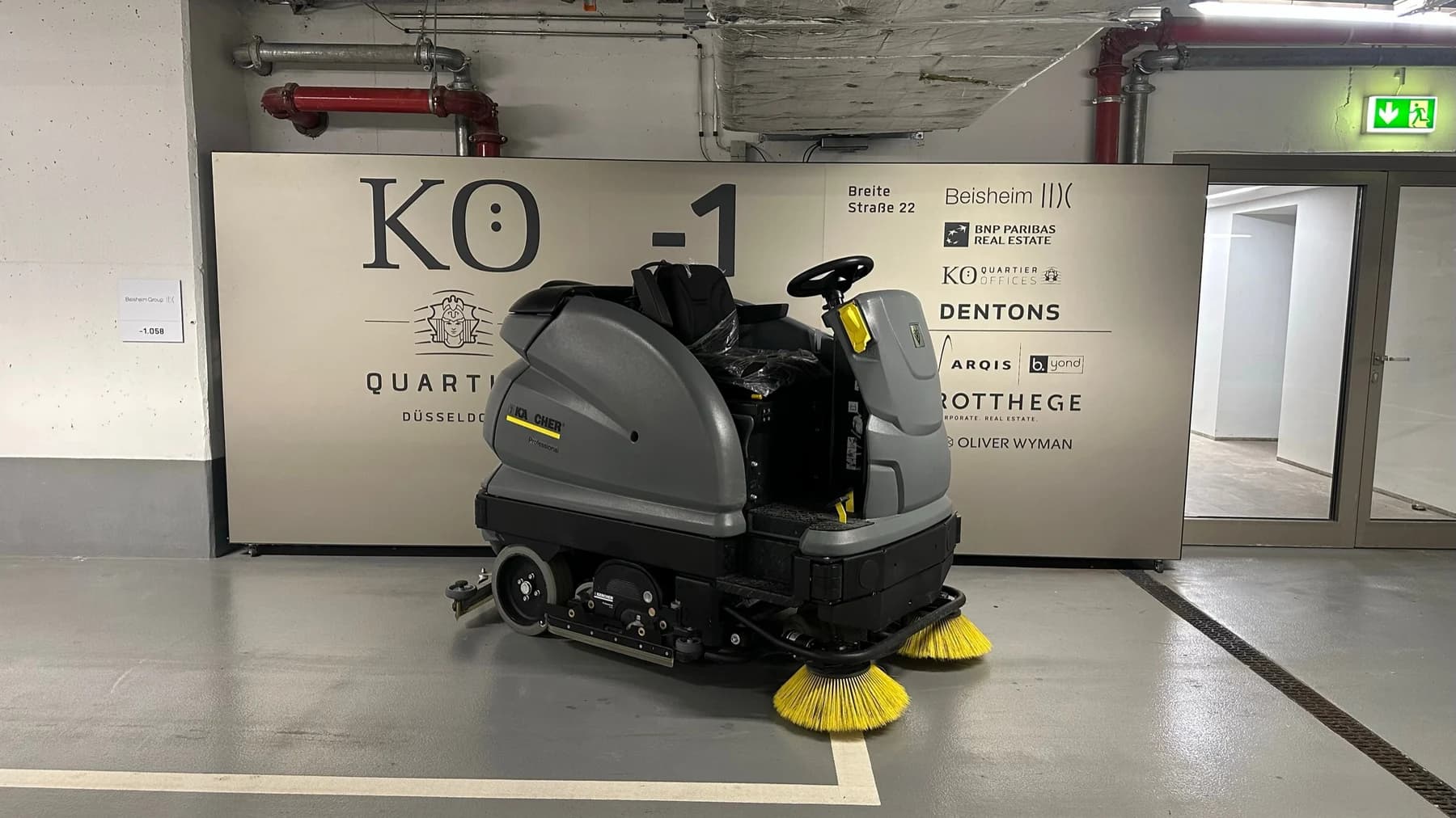 Aufsitz-Reinigungsmaschine mit seitlichen Bürsten auf dem Boden einer Tiefgarage.