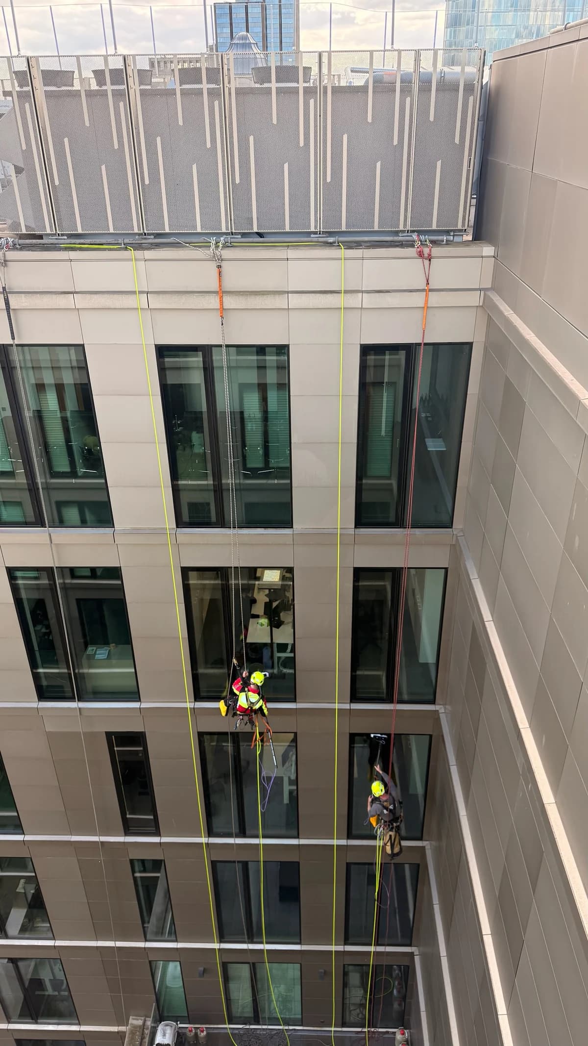 Blick von oben auf zwei seilgesicherte Personen an der Fensterfassade eines mehrgeschossigen Innenhofs.