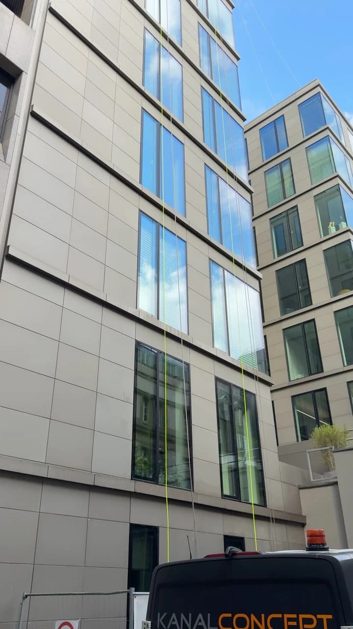 Blick entlang hoher Bürofenster, in denen sich der blaue Himmel spiegelt.
